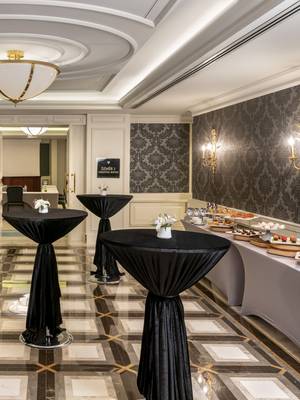Sophisticated foyer at Rixos Pera Istanbul with dark damask wallpaper, geometric tile floor, and black cocktail tables, set up for an event reception with a dessert buffet.